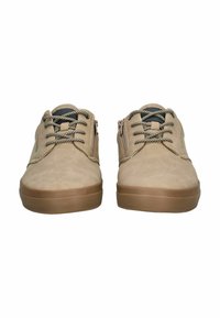 Une paire de chaussures décontractées beiges avec des lacets à motifs, des zips latéraux et des semelles en caoutchouc, montrée de face sur un fond blanc.