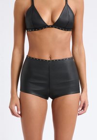 Set bikini nero composto da un reggiseno triangolare e pantaloni corti a vita alta, realizzato in materiale morbido con dettagli in metallo dorato lungo i bordi.