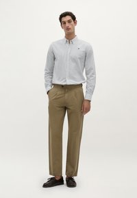 Camicia a righe blu chiaro e bianco, abbinata a pantaloni khaki. L'outfit è completato da scarpe marroni scure e una vestibilità rilassata.