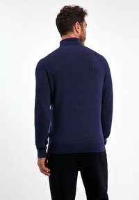 Granatowy sweter dziergany z wysokim kołnierzem, ściągaczowymi mankietami i brzegiem. Faktura materiału z dopasowanym krojem. Bez widocznych wzorów ani akcentów.