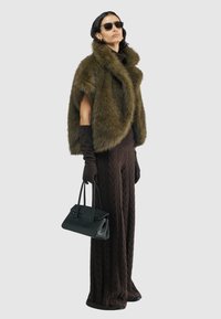 Olijfgroene nepbont cape, bruine gebreide coltrui, bruine kabelgebreide ruime broek, lange bruine handschoenen en een zwarte handtas.