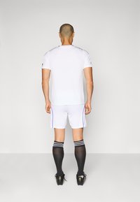 White athletic jersey and shorts with blue accents, paired with black knee-length socks featuring white stripes and black soccer cleats.