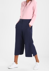 Rosa långärmad topp med knytning vid halsen, parat med marinblå culotter med sidslitsar. Bärs med vita sneakers.