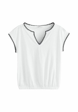 Witte blouse met korte mouwen met zwarte zigzagafwerking langs de halslijn en mouwranden en een elastische tailleband onderaan.