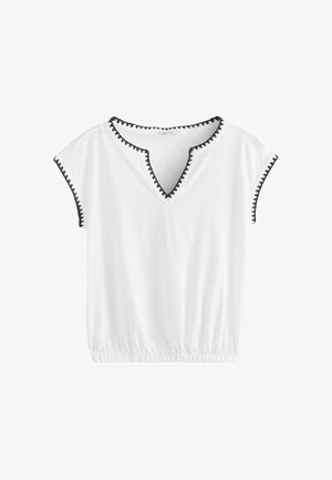Blouse blanche à manches courtes avec un galon zigzag noir le long de l'encolure et des bords des manches, et une ceinture élastique en bas.