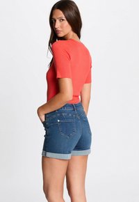 Aansluitende koraalkleurige ribbeltop en donkerblauwe denimshorts met opgerolde manchetten. De shorts zijn voorzien van achterzakken en een klassiek vijfzakendesign.