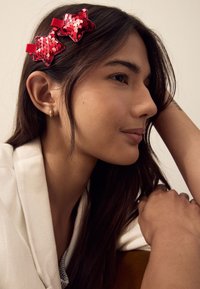Red sequin star-shaped hair clips with red fabric bands, worn in dark hair against a neutral background, complemented by a light-colored top.