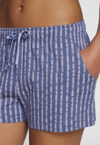 Pyjama-shorts laget av myk stoff i blått med et rosa horisontalt stripe-mønster. Har elastisk liv og sidelommer.