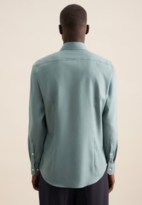 Chemise bleu-vert clair à manches longues, col classique et poignets à boutons, avec une texture lisse et un ourlet arrondi.