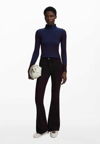 Lila és kék csíkos garbó, fekete bővülő fazonú nadrág, világoszöld kézitáska, fehér bebújós cipő.