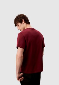 Bordeauxrotes Baumwoll-T-Shirt mit kurzen Ärmeln, Rundhalsausschnitt und lässigem Schnitt. Glatte Textur, keine sichtbaren Muster oder Akzente.