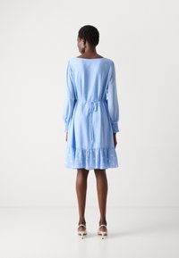 Lichtblauwe jurk met lange pofmouwen, stippenpatroon, strikceintuur en gerimpelde zoom. Glad textuur, knielengte, elegante uitstraling.