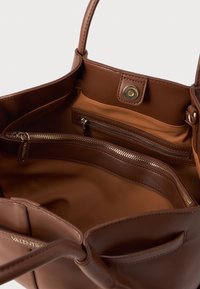 Bolsa tote de couro castanho com duas alças, bolsos interiores com fecho zip e um fecho de pressão dourado. Textura suave com um acabamento mate.