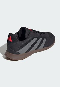Zwarte sportieve schoen met een gestructureerde bovenkant, voorzien van grijze strepen, rode accenten en een rubberen zool. Ontworpen voor prestaties en comfort.