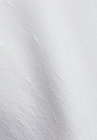 Biała, teksturowana tkanina z delikatnym wzorem. Powierzchnia ma małe, podniesione akcenty, co nadaje jej jakość dotykową.