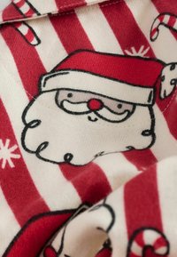 Rot-weiß gestreifter Stoff mit einer Illustration des Weihnachtsmannes, der einen roten Hut, einen weißen Bart, schwarze Linien und Zuckerstangen-Akzente zeigt.