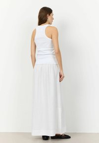 Wit mouwloos tanktopje gecombineerd met een lange, vloeiende witte rok, met een subtiele textuur en een zijsplit, en zwarte gevlochten ballerina's.