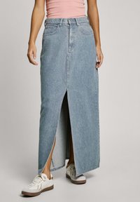 Lichtblauwe denim maxi rok met een voorkeursplit, hoge taille en klassiek vijf-pocketdesign, gecombineerd met witte sneakers.