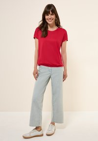 Rode T-shirt met korte mouwen en een ronde hals, gecombineerd met lichtblauwe wijde jeans en witte sneakers met tan accenten.