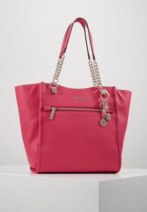 Sac à main Guess en cuir rose vif avec anses chaîne dorée, poche avant zippée, logo en métal et détails charmants sur une surface blanche.