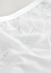 Vêtement blanc avec un panneau en dentelle texturée à motifs floraux et un tissu lisse en dessous, bordé d'une taille souple et plate.