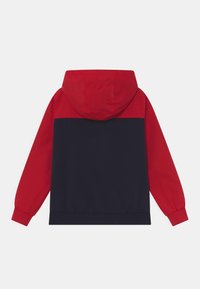 Kraťas s kapucí, který má červenou horní část a tmavě modrou spodní část. Měkká tkanina s elastickými manžetami a pásem pro příjemné nošení.