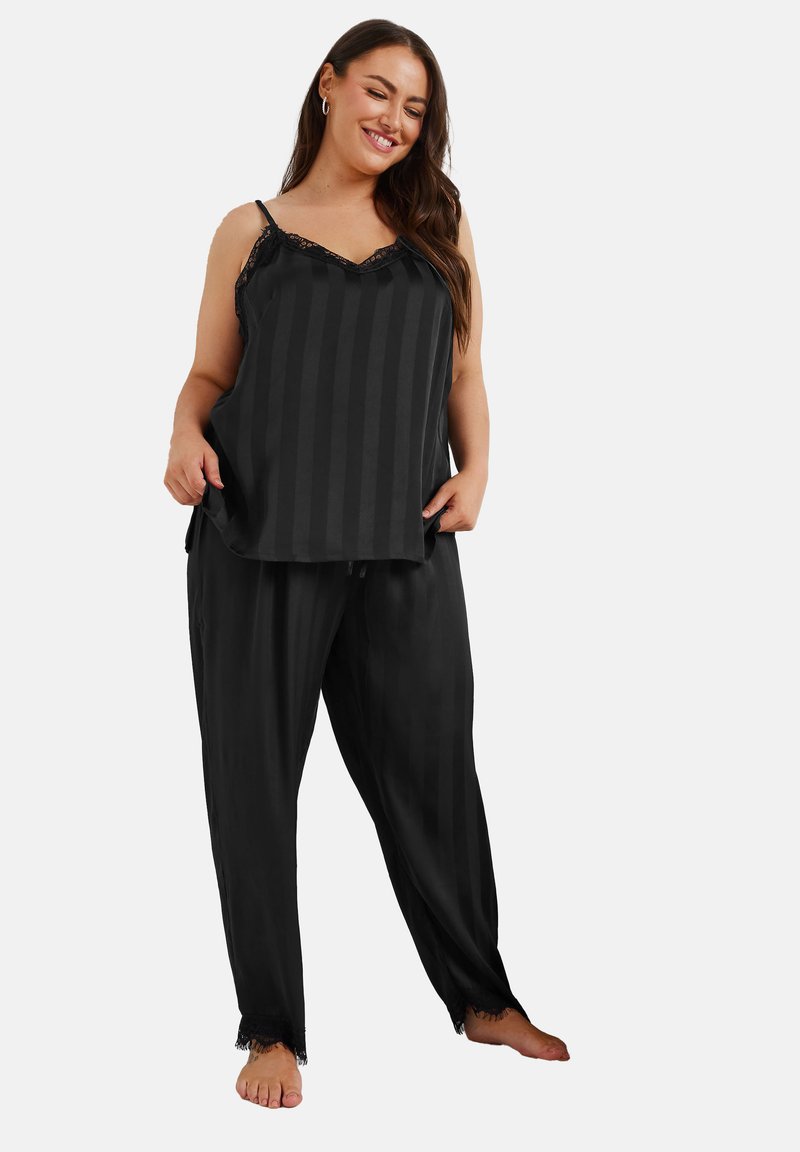 Svart satin pyjamasset som består av en ärmlös topp med spetsdetaljer och randigt mönster, kombinerad med löst sittande randiga byxor.