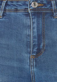 Jeans de mezclilla en un lavado azul medio con costuras naranjas en contraste, que cuentan con un cierre frontal de botón y un diseño de bolsillo detallado.