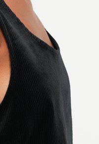 Top fără mâneci, de culoare neagră, cu o croială relaxată și decolteu larg, fabricat dintr-un material texturat, fără elemente metalice vizibile.