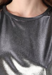 Top grigio metallico lucido con una superficie liscia e un colletto rotondo, che mostra riflessi di luce e una lucentezza sottile sulla stoffa.