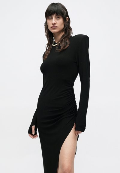 Μαύρο φόρεμα με μακριά μανίκια και εφαρμοστή γραμμή, με πτυχώσεις στο πλάι και ψηλή σκίσιμο στην αριστερή πλευρά. Κατασκευασμένο από λεία, ελαστική ύφανση.