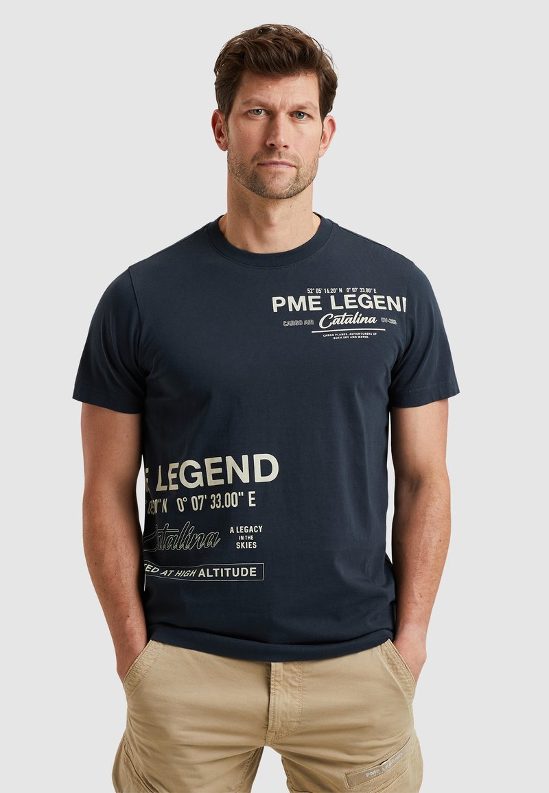 T-shirt en coton bleu marine avec texte imprimé blanc et coordonnées. Col rond, manches courtes, coupe décontractée et texture lisse.