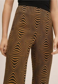 Pantaloni marroni e neri con motivo a linee ondulate. Il tessuto strutturato crea un effetto visivo audace attraverso forme geometriche.