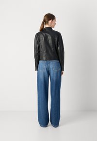 Kratka jakna iz črne usnje s prilegnjenim dizajnom, v kombinaciji z visokimi širokimi hlačami iz modrega denima, ki imajo zadnje žepe.