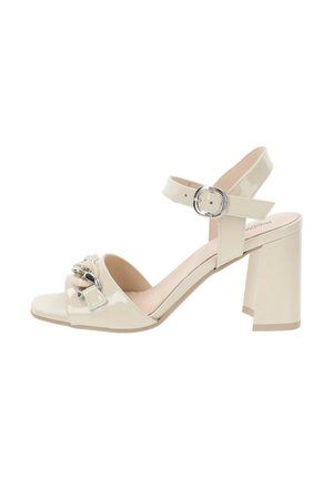 Sandali con tacco alto in pelle patente beige, con tacco a blocco, cinturino alla caviglia regolabile e un fiocco decorativo con dettagli metallici sulla punta.