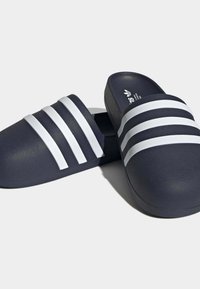 Sandales à glissière bleu marine en caoutchouc texturé, avec trois bandes blanches horizontales sur le dessus et une semelle arrondie.