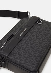 Zwarte leren schoudertas met een monogrampatroon, zilverkleurige hardware en een afneembare schouderband. Ritssluiting met logo-detail.