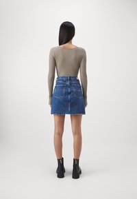 Ribbad långärmad topp i taupe, i kombination med en blå denim minikjol med fransad nederkant, bärs med svarta ankle boots med logotypdetaljer.