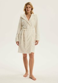 Biały, kapturowy szlafrok z fakturowanej tkaniny w jodełkę; związywany pasek w talii; długie rękawy; miękka struktura; sięga do połowy łydki.