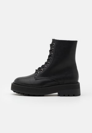 Bottines en cuir noir avec un bout arrondi, une semelle plate et un laçage à l'avant. Elles présentent des œillets en métal et un dessus texturé.