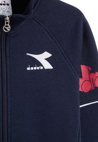 Giacca zip-up blu navy realizzata in tessuto strutturato; presenta un logo ricamato bianco e grafiche rosse sulla manica.