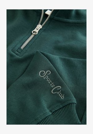 Sudadera de cremallera verde oscuro hecha de tela suave. Presenta una cremallera plateada y texto bordado "Club Deportivo" en la manga.