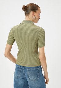 Polo a maglia verde a coste con maniche corte, dotato di colletto classico e design aderente, abbinato a jeans in denim blu a vita alta.