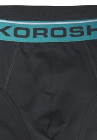 Schwarze Unterwäsche mit einem türkisfarbenen Bund, auf dem "KOROSH" in Schwarz gedruckt ist. Glattes Material mit eng anliegendem Schnitt und elastischem Taillenbund.