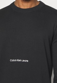 Svart crewneck-tröja i mjukt tyg med vitt broderat "Calvin Klein Jeans"-logotyp på bröstet.