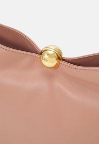 Sac en cuir rose blush avec une finition texturée ; dispose d'un fermoir sphérique doré proéminent avec logo en relief. Design doux et structuré.