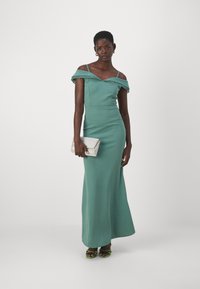 Rochie mint green, fără umeri, cu dantelă la margini, siluetă mulată și lungime mare. Asortată cu o poșetă argintie și sandale verzi.
