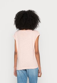 Paalroze top met korte mouwen, losse pasvorm en ronde hals. De stof heeft een zachte textuur, zichtbaar vanaf de achterkant. Gecombineerd met een blauwe spijkerbroek.