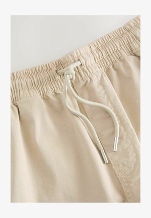 Shorts beige a vita elastica con cordino. Il tessuto è liscio e leggero, con terminali argentati sul cordino.