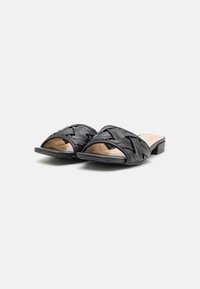 Svarta platta sandaler med vävda läderremmar och öppen tå på vit bakgrund.